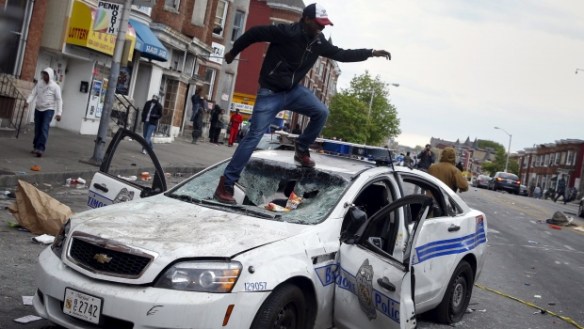 Demonstrators jump on a damaged Baltimore police department vehicle during clashes in Baltimore